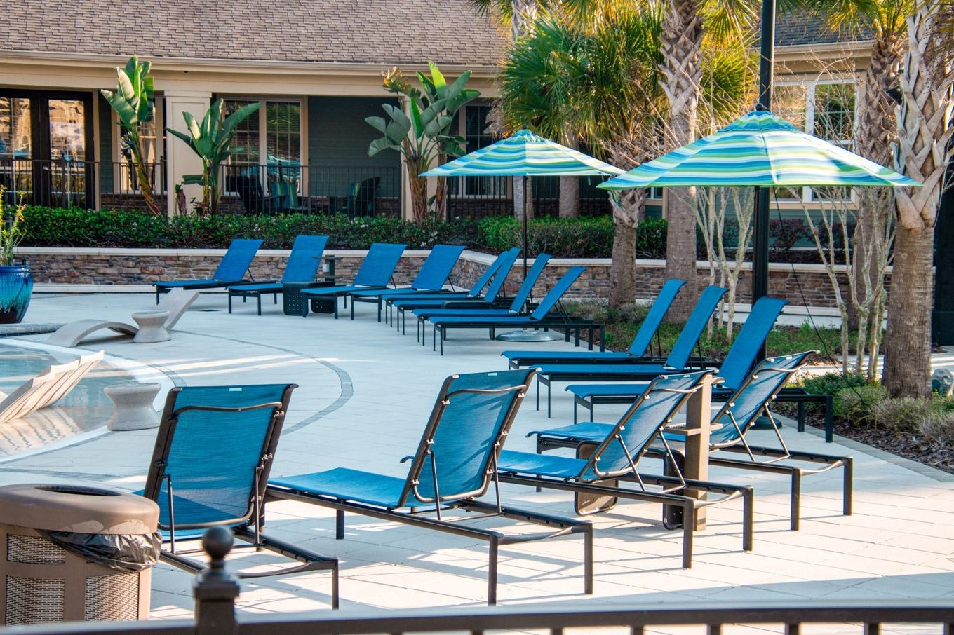 An apartment complex pool with blue lounge chairs and umbrellas